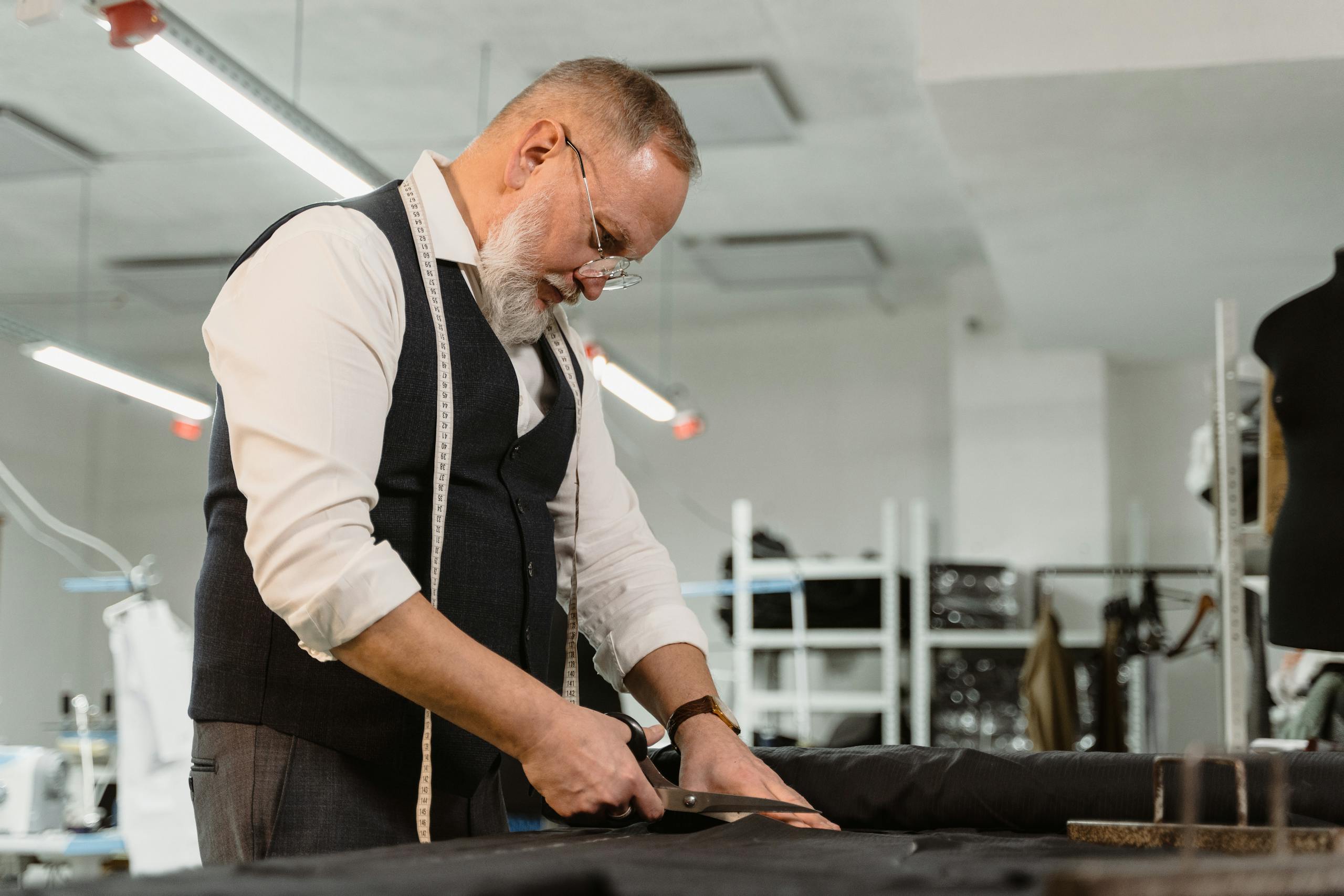 A professional tailor focused on cutting fabric for a luxury suit in an atelier.